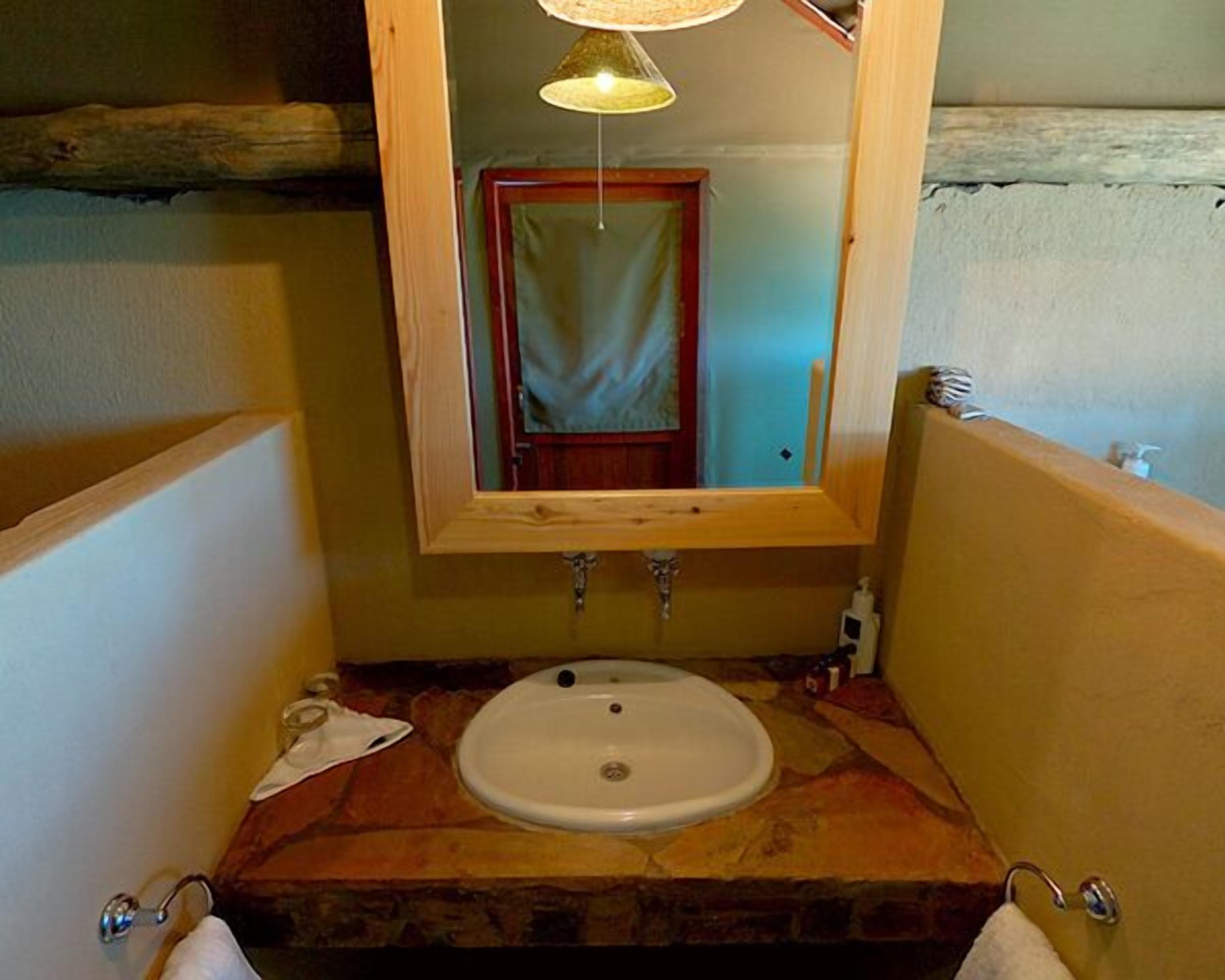 Casa de banho com lavatório de pedra, espelho com moldura de madeira e luminária suspensa.
