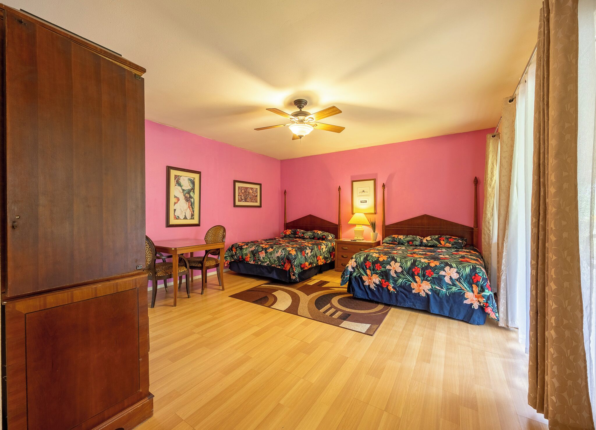 Una habitación con dos camas, un armario de madera, un escritorio con silla y un ventilador de techo.