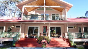 A two-story building with a red roof, a balcony on the upper floor, and a front porch with steps leading to the entrance.