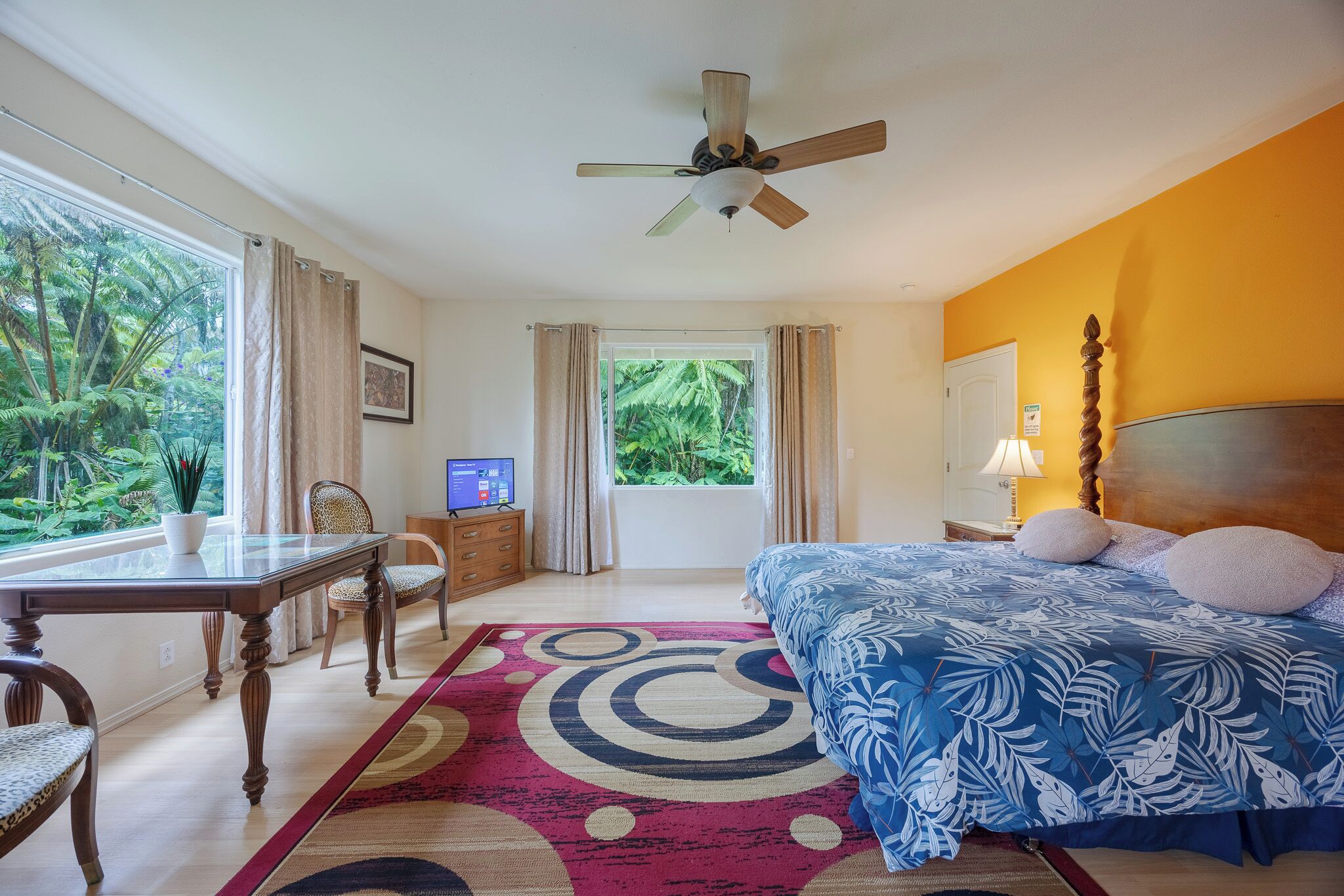 A bedroom with a bed, a desk, a chair, a television, and a window with curtains.