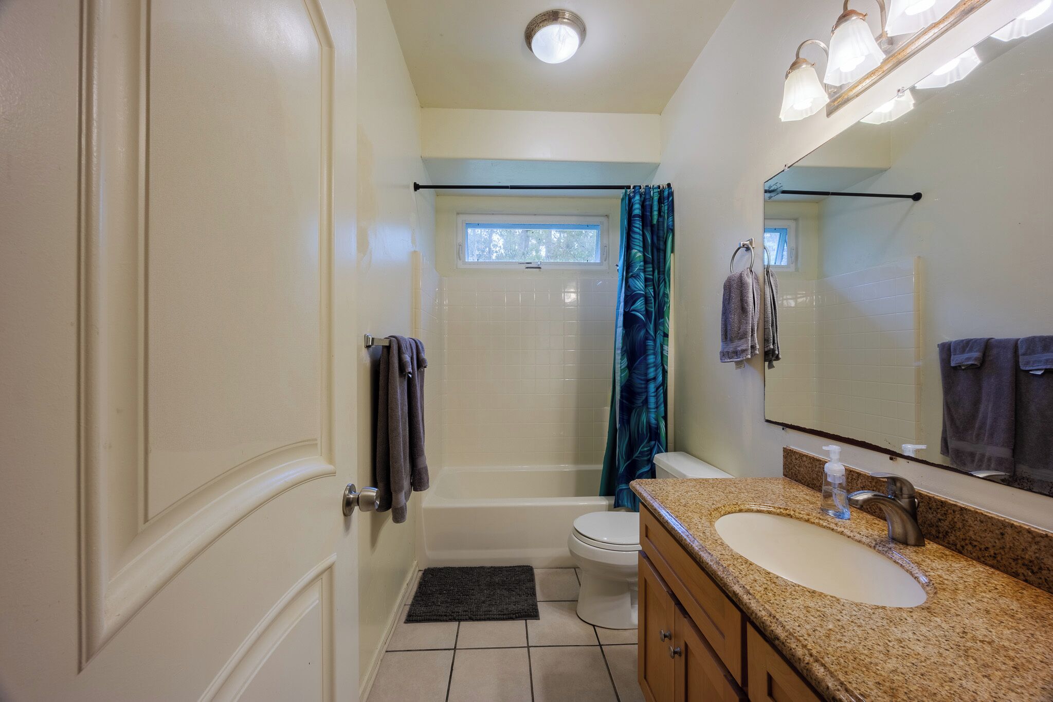 A bathroom with a bathtub, toilet, sink, and a window above the shower.