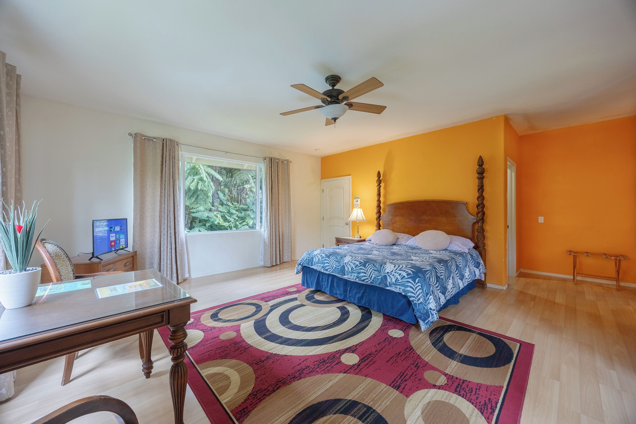 Un dormitorio con cama, escritorio, computadora, ventilador de techo y ventana con cortinas.