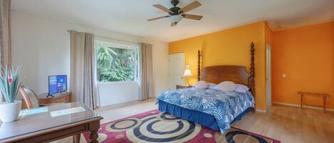 A bedroom with a bed, a desk, a computer, a ceiling fan, and a window with curtains.