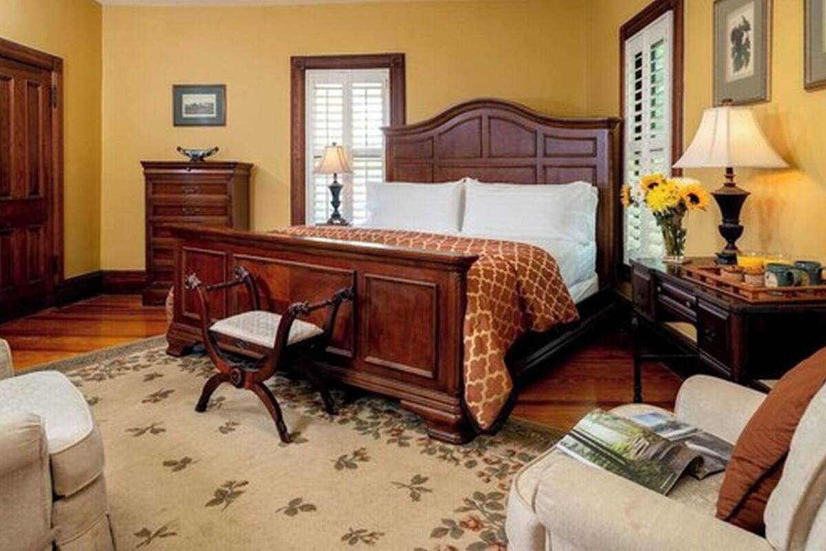 A bedroom with a large bed, wooden furniture, a floral rug, and a window with shutters.