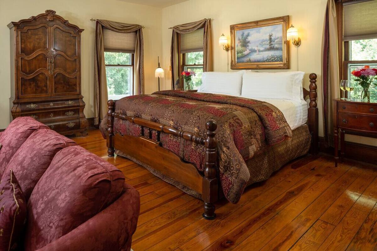 A traditional bedroom with a wooden four-poster bed, a large wooden wardrobe, and a painting on the wall.