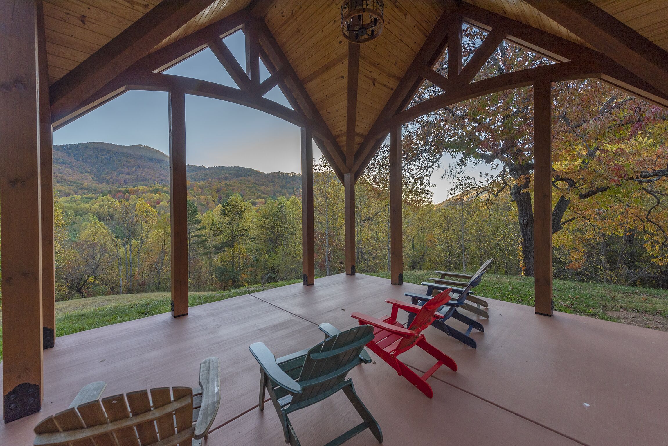 Ein überdachter Außenbereich mit Adirondack-Stühlen und Blick auf einen bewaldeten Hügel.