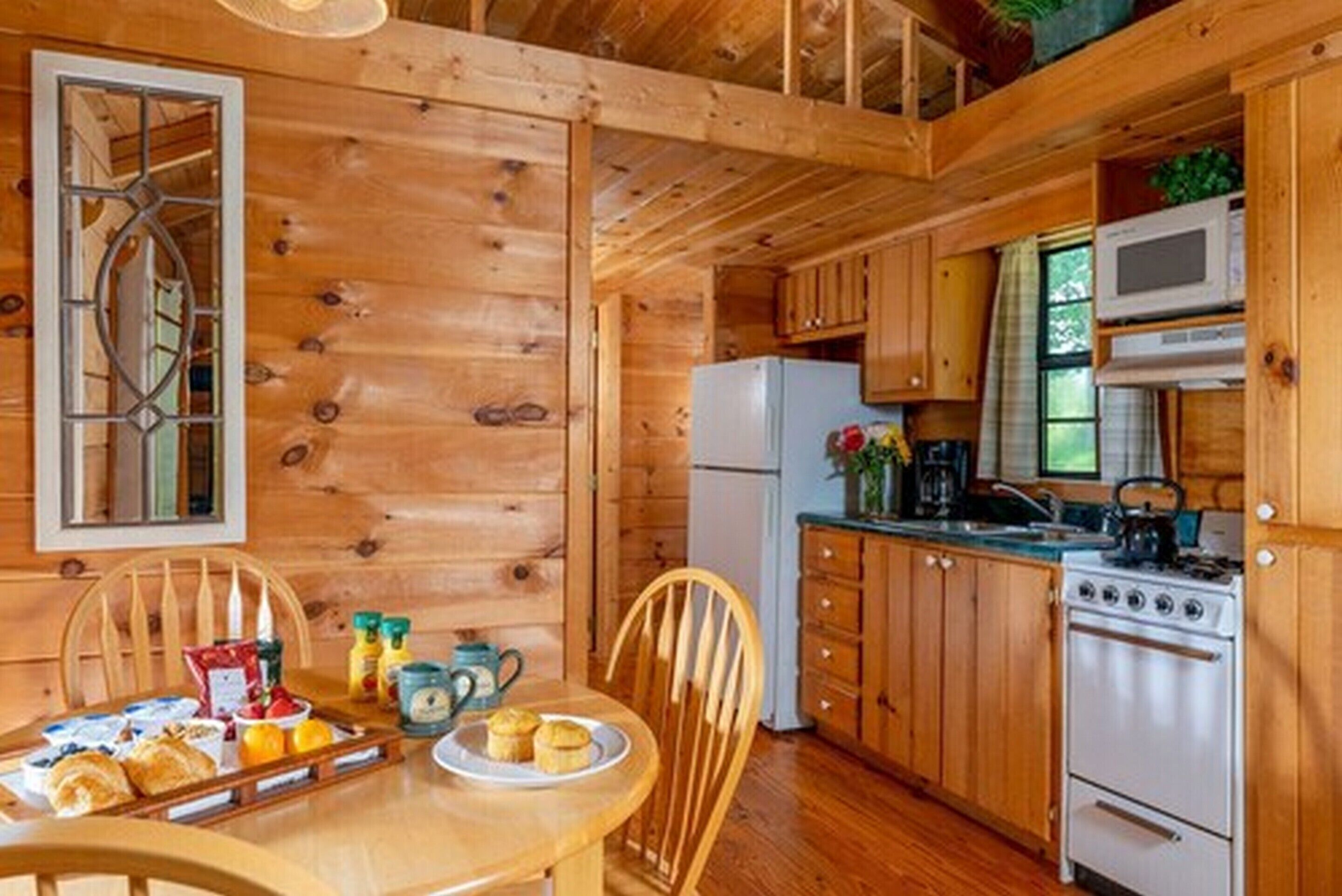 A wooden cabin interior with a dining table set with breakfast, a refrigerator, a stove, and wooden cabinets.