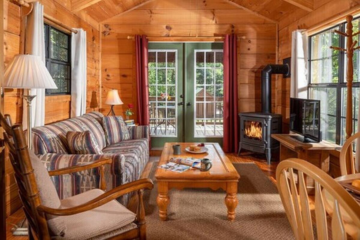 A cozy log cabin interior with a sofa, chairs, a coffee table, a fireplace, and a television.