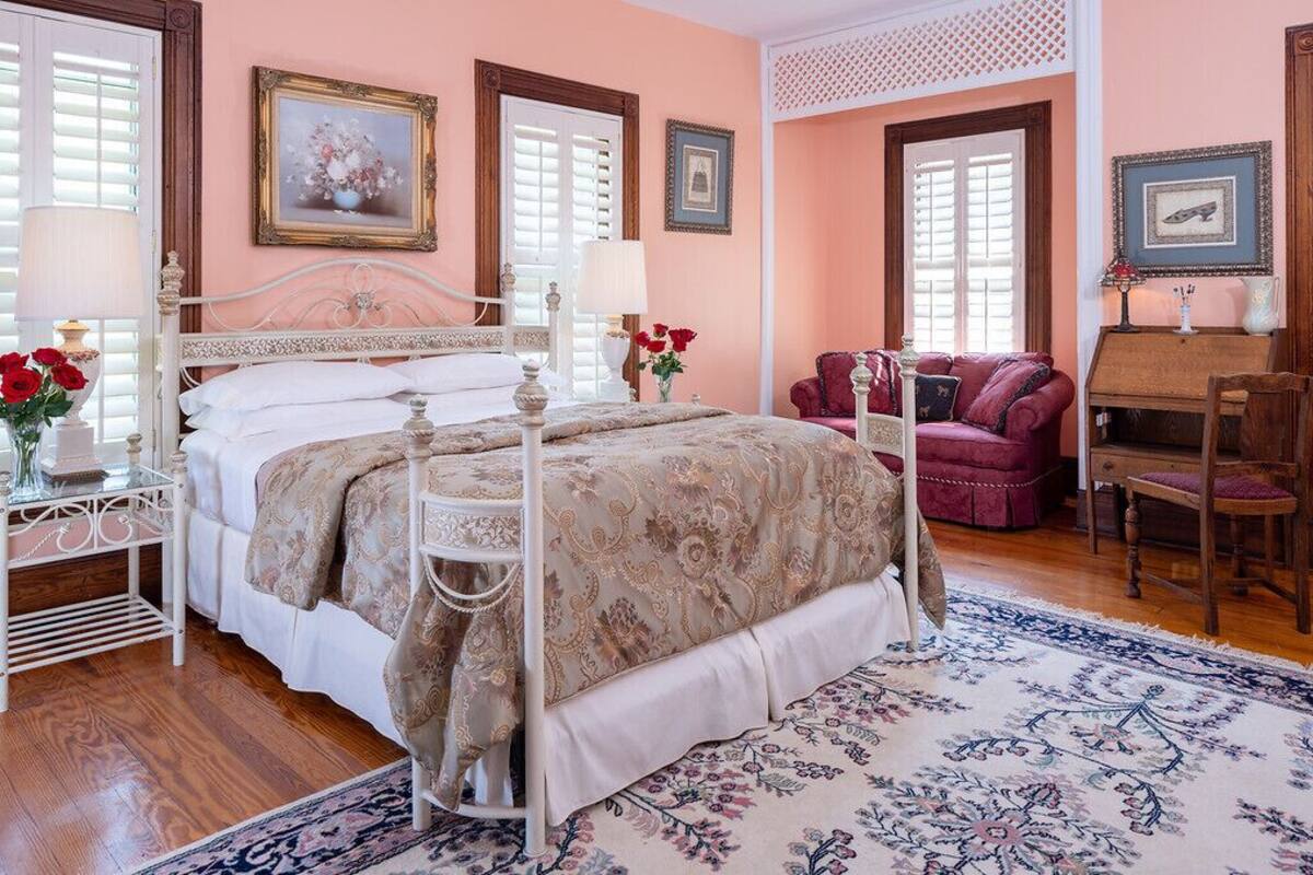 A bedroom with a four-poster bed, a sitting area with a red sofa, and a wooden piano.