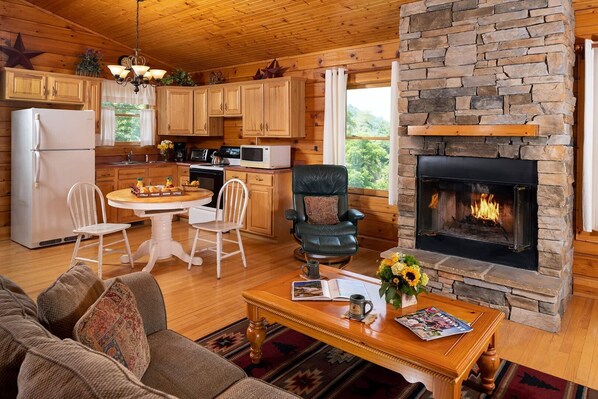 Interior acogedor de una cabaña con chimenea de piedra, muebles de madera y una zona de cocina.
