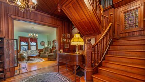 Un vaste salon agrémenté d’un magnifique escalier, d’un parquet en bois et d’un grand piano.