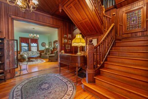 Uma sala de estar ampla com uma escadaria imponente, piso de madeira e um piano grande.
