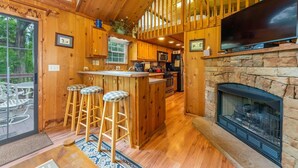 A wooden cabin interior with a kitchen, bar stools, a fireplace, and a television. - Engadine Inn & Cabins (Candler)
