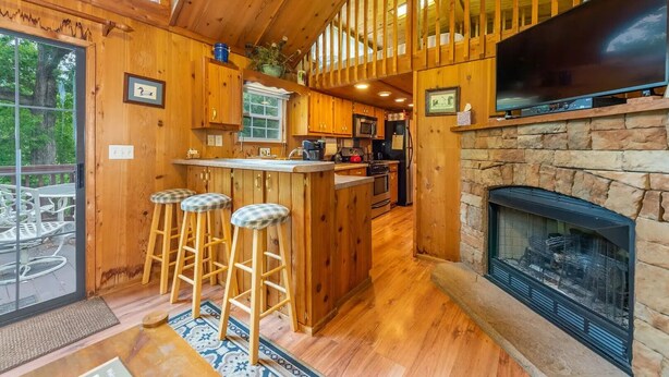 L’intérieur d’un chalet en bois comprend une cuisine, des tabourets de bar, une cheminée et un téléviseur.