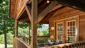 Une cabane en bois dotée d’un porche abrité, d’une table à manger avec des chaises, et offrant une vue sur la forêt environnante.