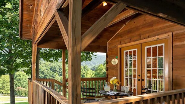 A wooden cabin with a covered porch, a dining table with chairs, and a view of the surrounding forest. - Engadine Inn & Cabins (Candler)