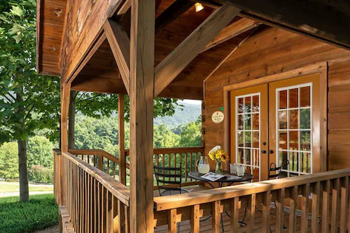 A wooden cabin with a covered porch, a dining table with chairs, and a view of the surrounding forest.