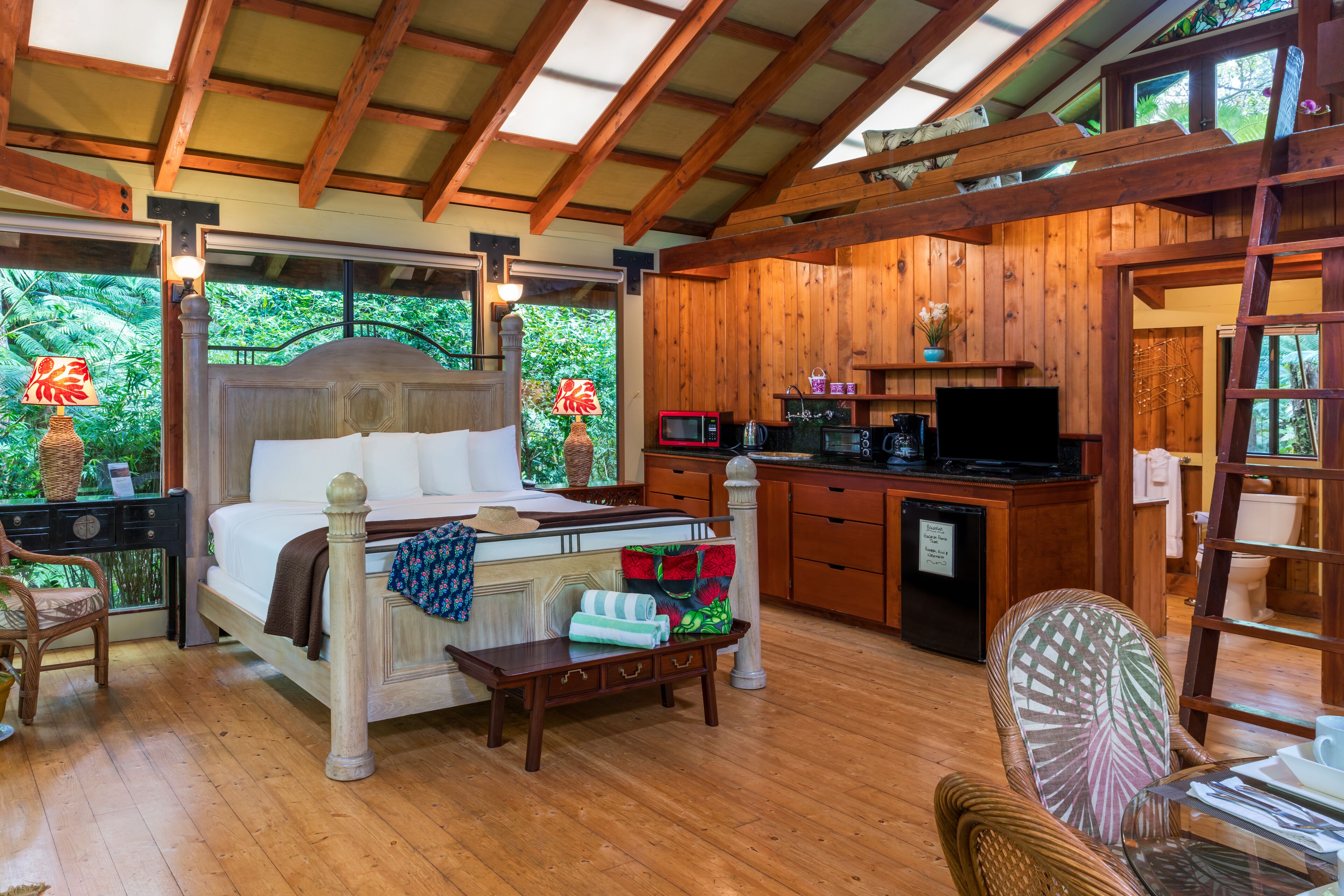 A wooden room with a bed, a desk, a chair, a small table, and a television.