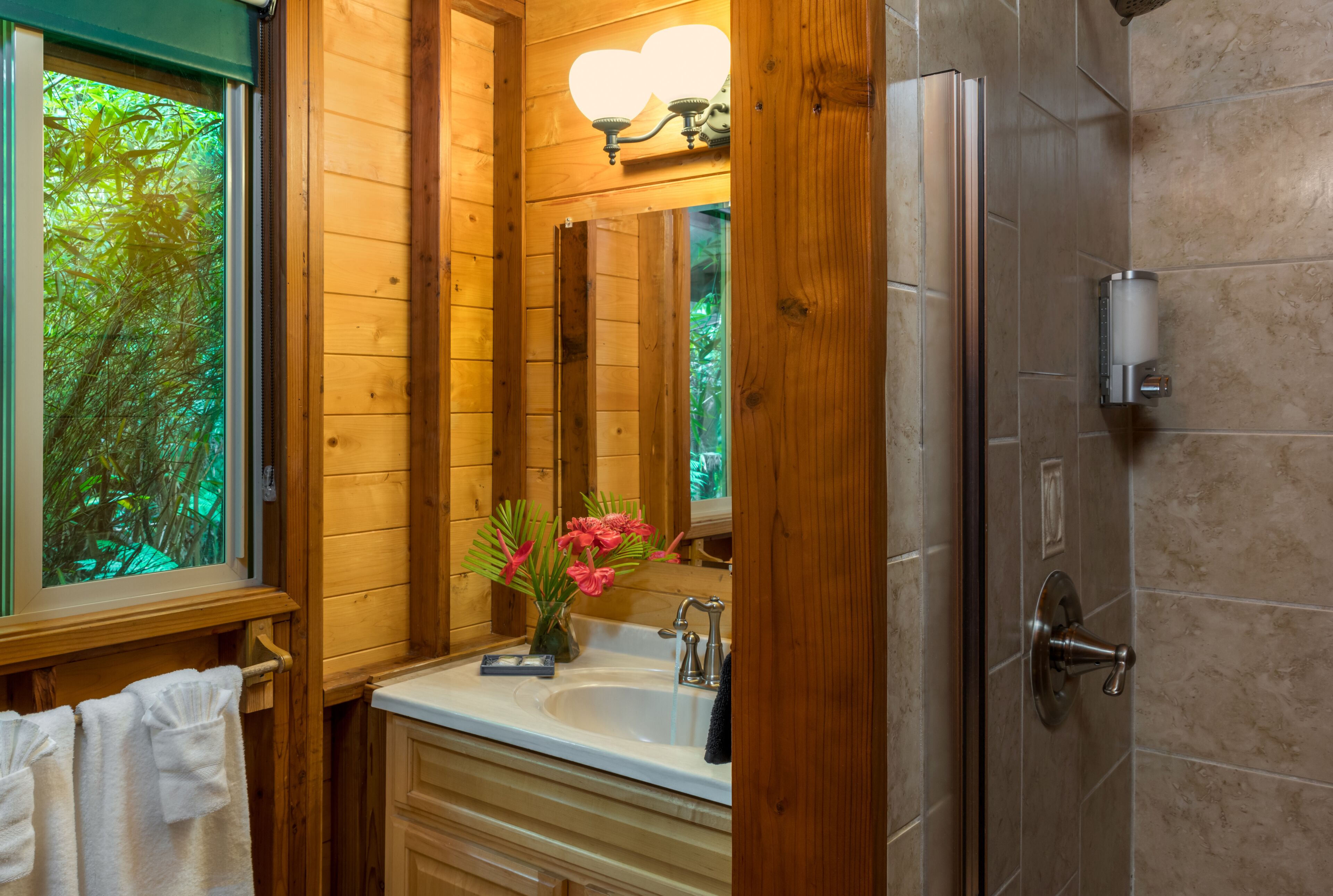 A wooden bathroom with a sink, mirror, and shower.