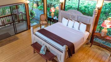 Un dormitorio amplio con una cama grande, suelo de madera y vistas a un follaje exuberante a través de amplias ventanas.