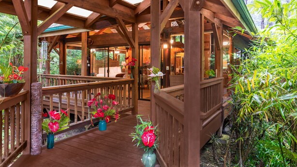 A wooden deck with a wooden railing, surrounded by potted plants and flowers. - Volcano Village Lodge (Volcano)
