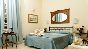 Habitación de hotel con cama, una mesita con tetera, espejo y un cuadro en la pared.