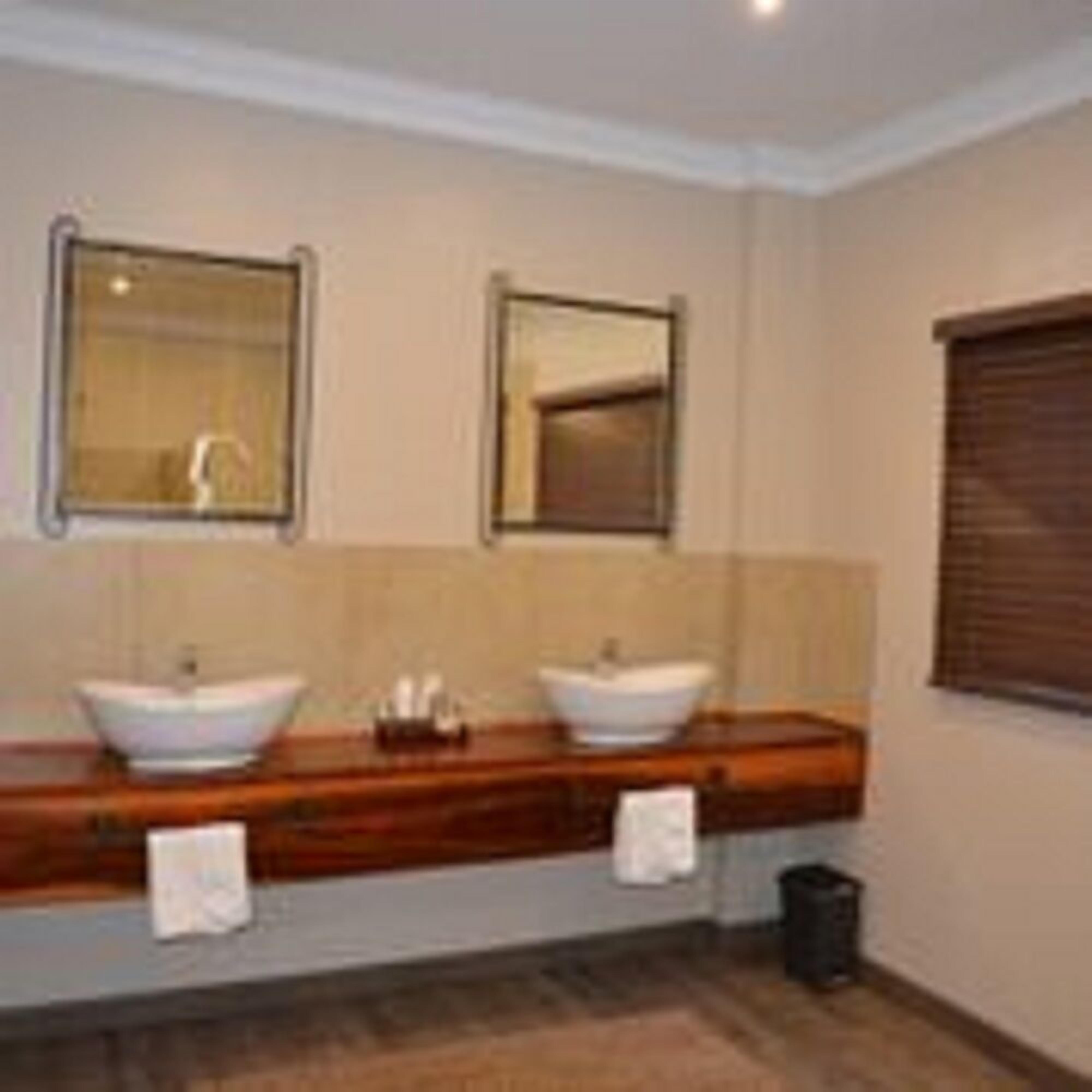 A bathroom with two sinks, a mirror above each, and a window with blinds.