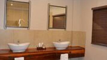 A bathroom with two sinks, a mirror above each, and a window with blinds.