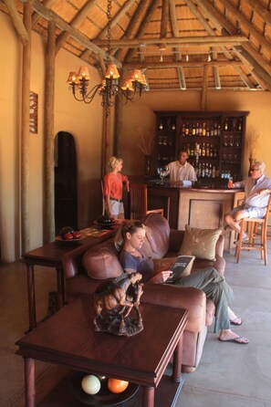 A cozy lounge area with a wooden table, leather sofa, and a bar with bottles. - Zebra Kalahari Lodge (Intu Afrika Kalahari Private Reserve)