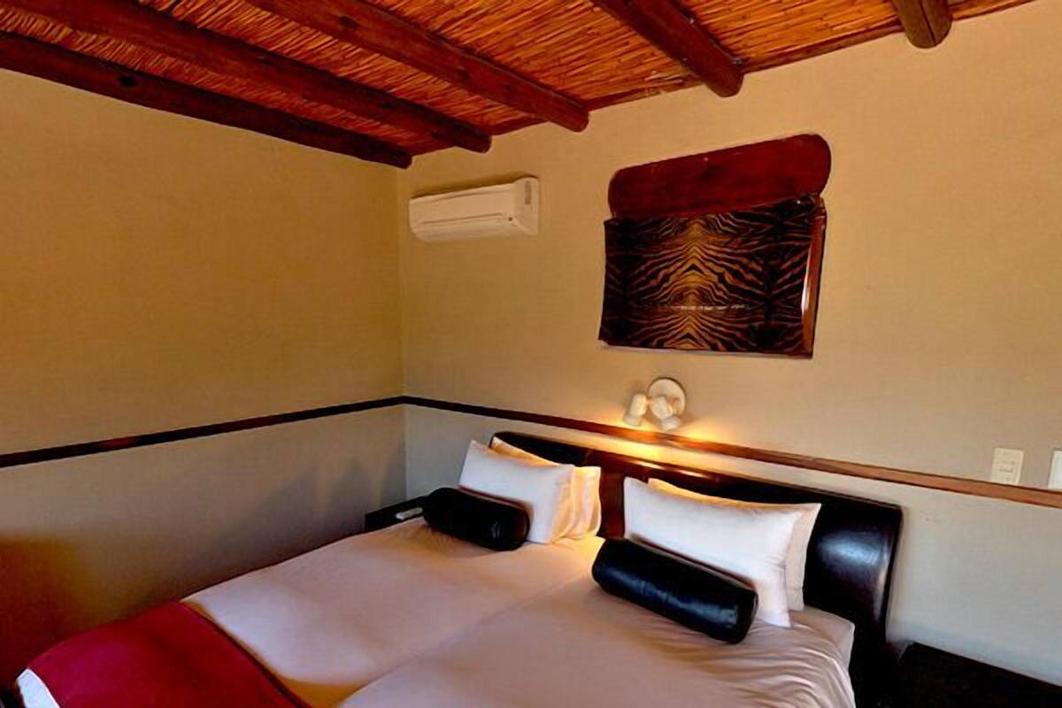 Une chambre d’hôtel avec un lit, un plaid rouge, un climatiseur fixé au mur et un élément décoratif mural.