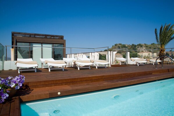 A rooftop pool area with lounge chairs and a modern building in the background.