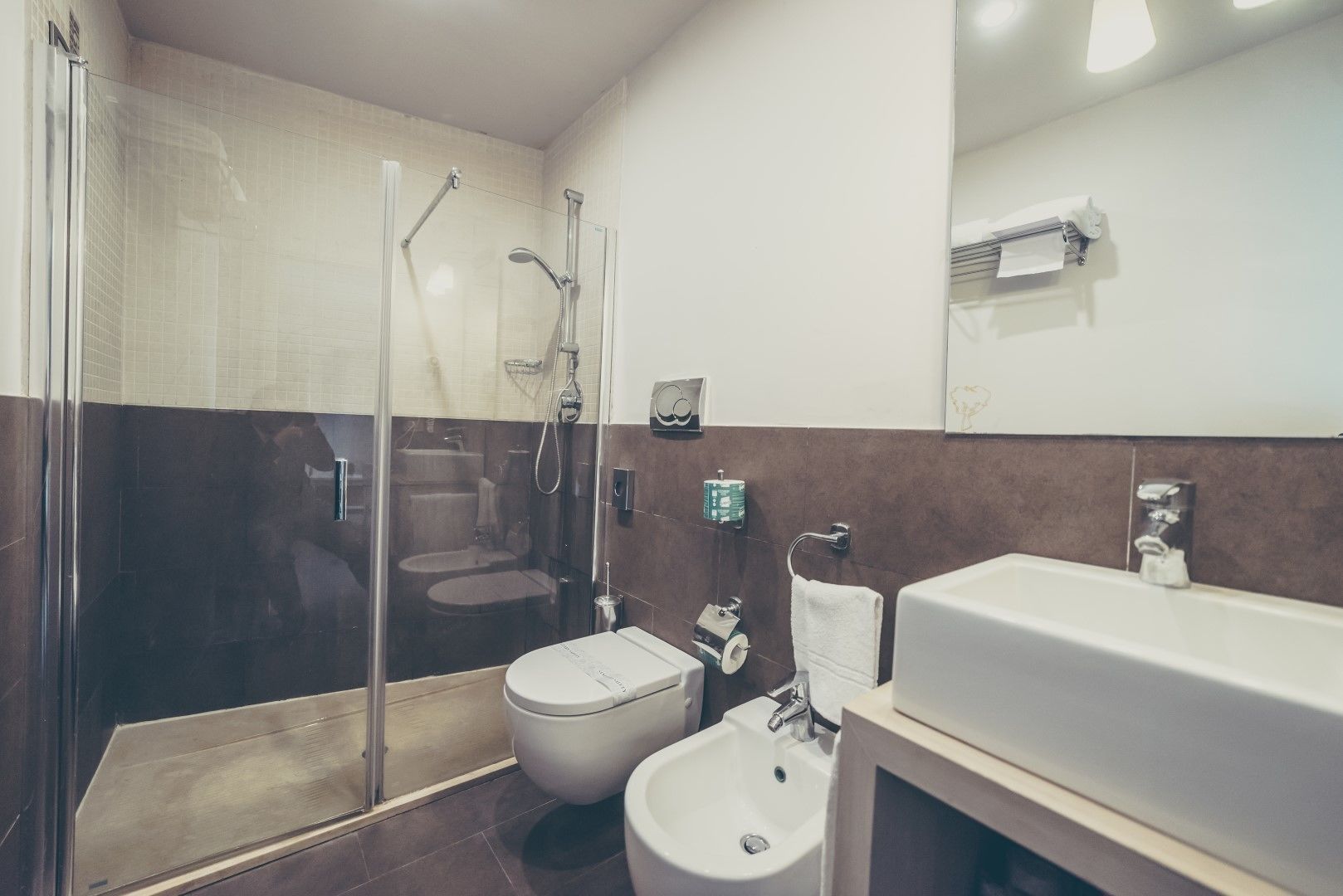 A modern bathroom with a glass-enclosed shower, a toilet, a bidet, and a sink.
