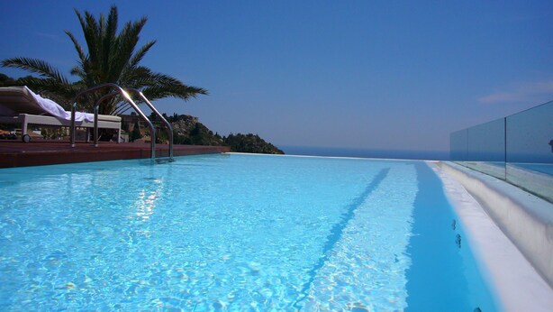 A clear blue pool with a palm tree and a lounge chair, surrounded by a clear sky. - Hotel Il Piccolo Giardino (Taormina)
