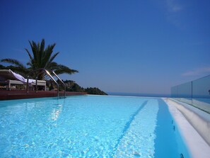 A clear blue pool with a palm tree and a lounge chair, surrounded by a clear sky.