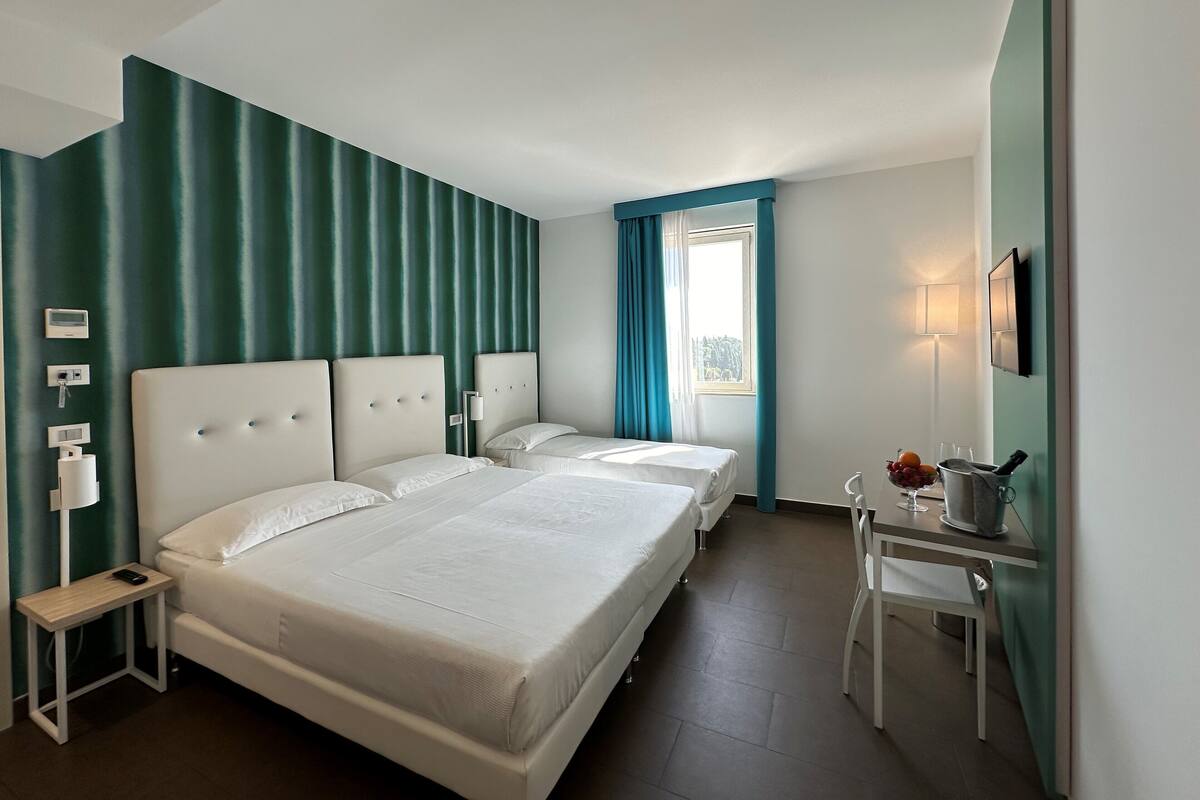 Une chambre d’hôtel avec deux lits, une petite table ornée d’un vase de fleurs et une fenêtre avec des rideaux.