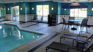 An indoor swimming pool with tiled flooring, seating areas, and a ceiling fan.