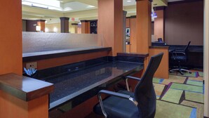 A hotel reception area with a counter, a single office chair, and a patterned carpet.