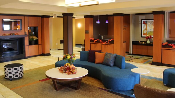 A modern hotel lobby with a fireplace, a blue sofa set, a round coffee table, and a small round table.