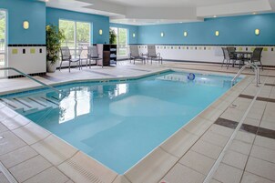 Una piscina interior con agua cristalina, rodeada de sillas de descanso y un suelo de baldosas.