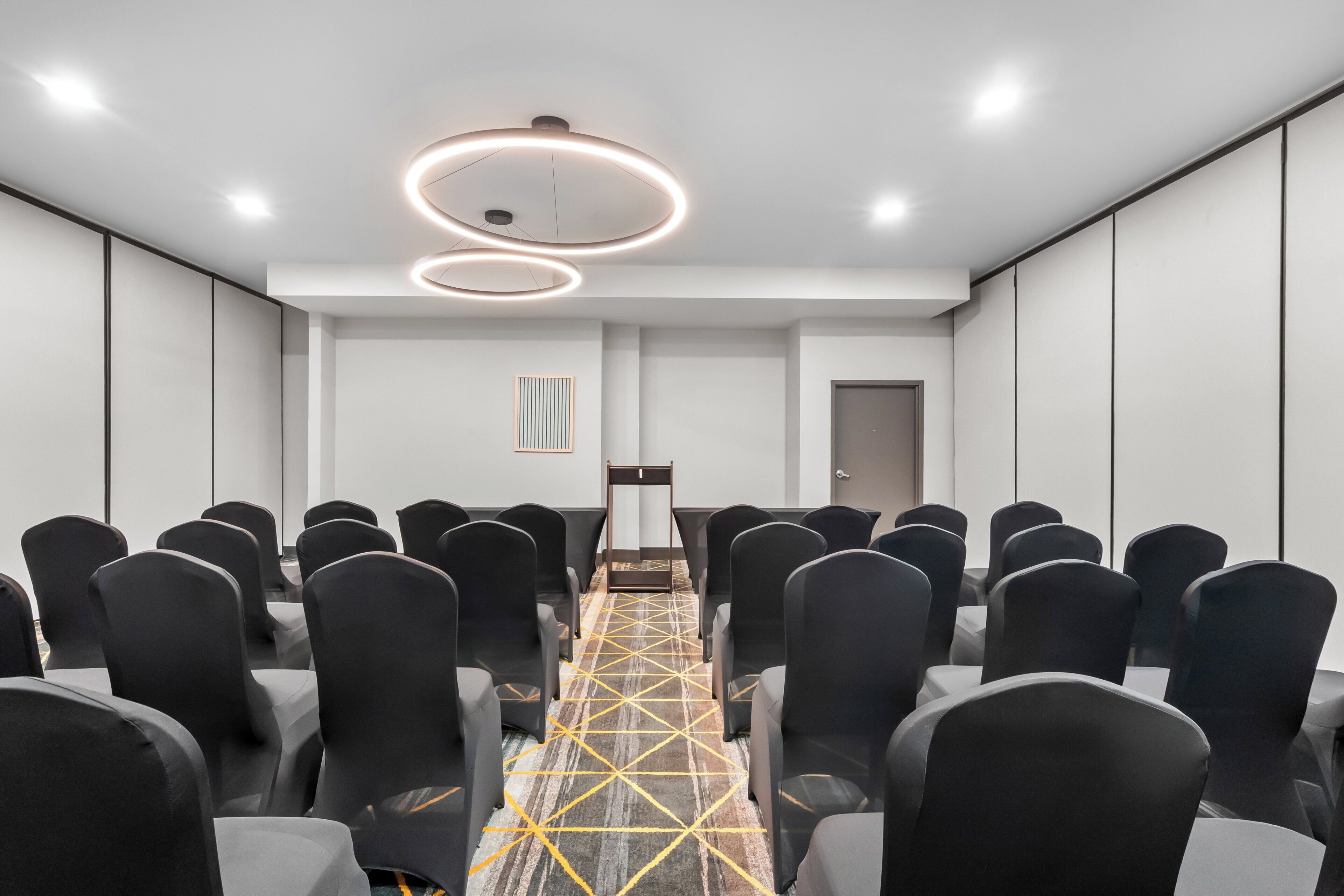 Un salón de conferencias con filas de sillas, una mesa central y luminarias modernas.