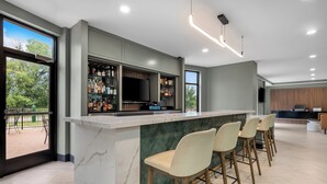 A modern bar area with a marble countertop, bar stools, a television, and a view of the outdoors. - Holiday Inn Oklahoma City Airport by IHG (Oklahoma City)