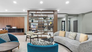A modern living room with a sofa, armchairs, a coffee table, and a bookshelf. - Holiday Inn Oklahoma City Airport by IHG (Oklahoma City)