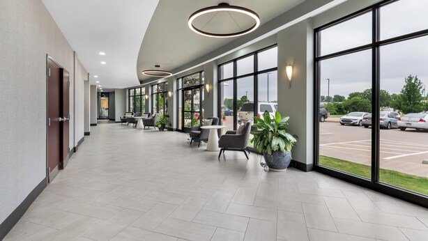 A spacious hallway with large windows, recessed lighting, and seating areas with potted plants. - Holiday Inn Oklahoma City Airport by IHG (Oklahoma City)