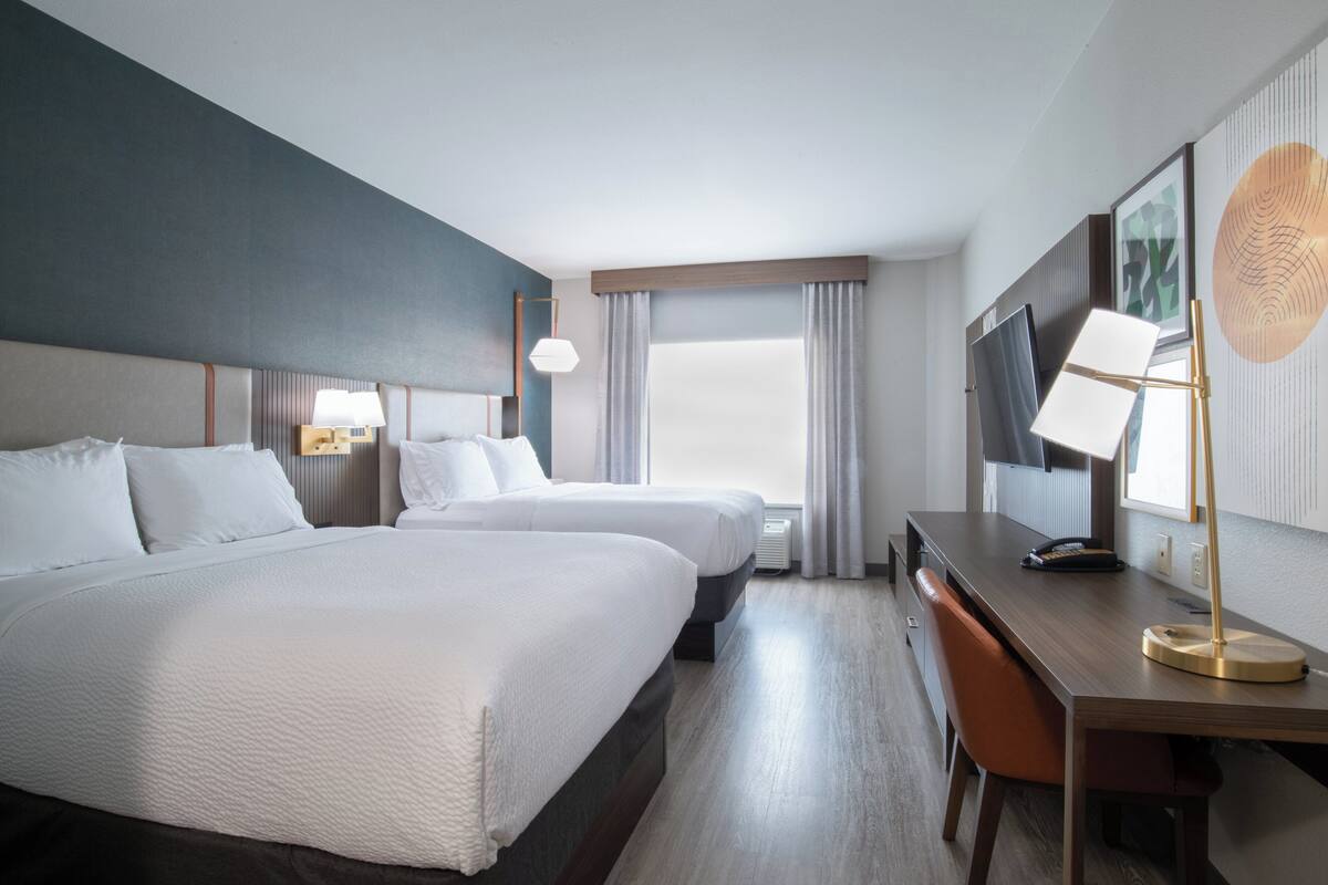 A hotel room with two beds, a desk, and a TV.