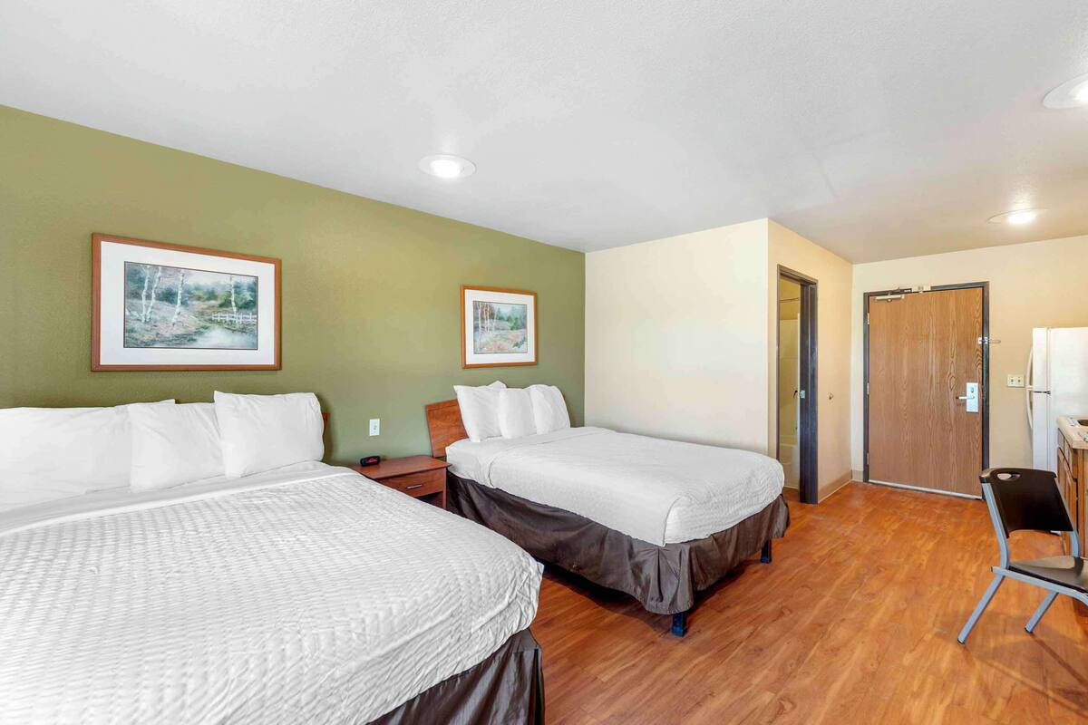 Ein Hotelzimmer mit zwei Betten, einem Schreibtisch, einem Stuhl und zwei gerahmten Bildern an der Wand.