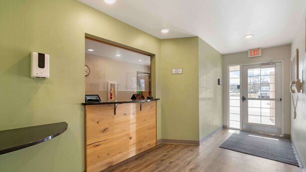 A reception area with a wooden counter, a clock, and an exit sign. - Extended Stay America Select Suites - Cincinnati - Florence - Airport (Florence)