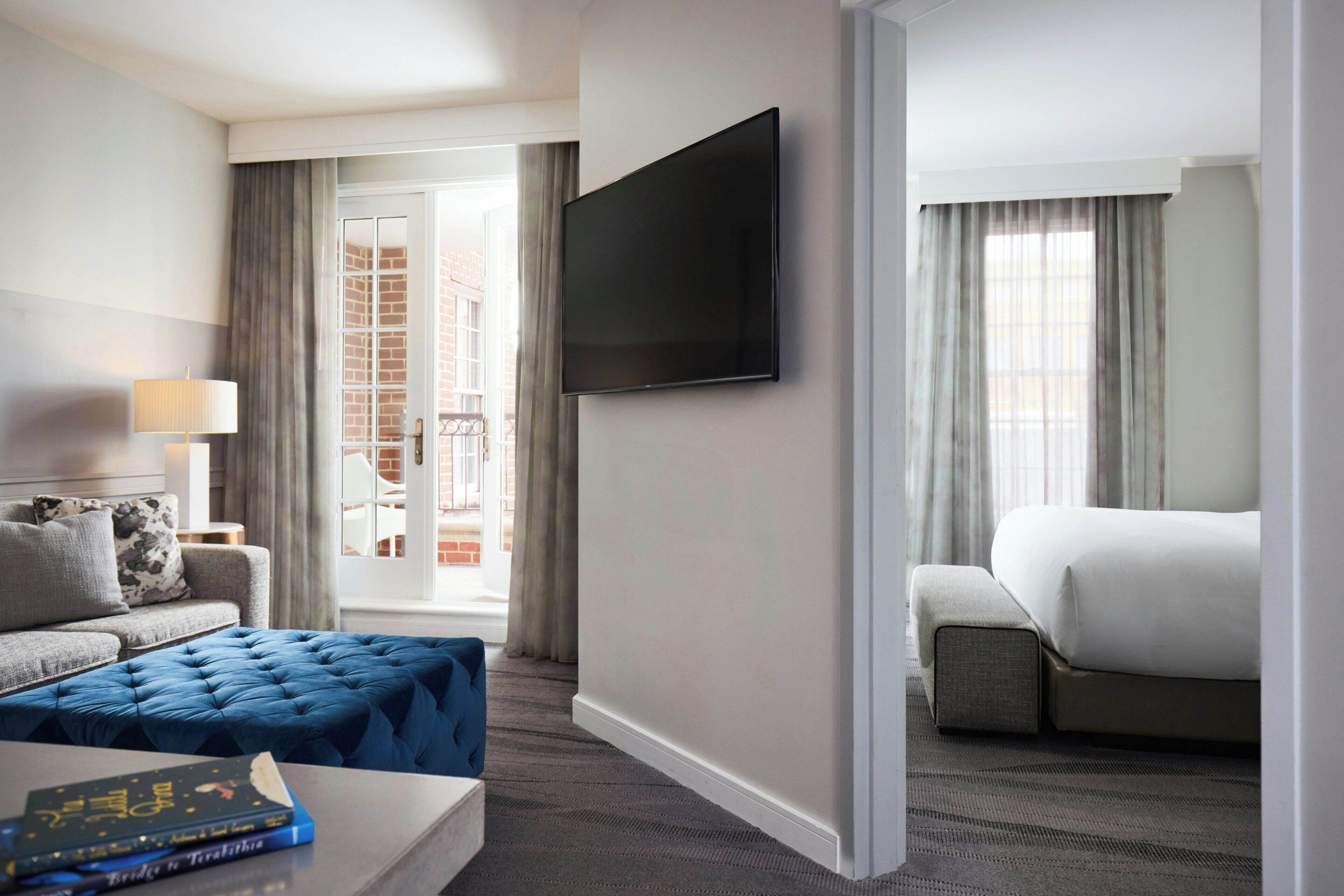 A hotel room with a flat-screen TV, a sofa, a bed, and a view of a building through the window.
