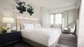 Habitación de hotel con una cama grande, una mesita de noche con lámpara, una silla y un cuadro en la pared.