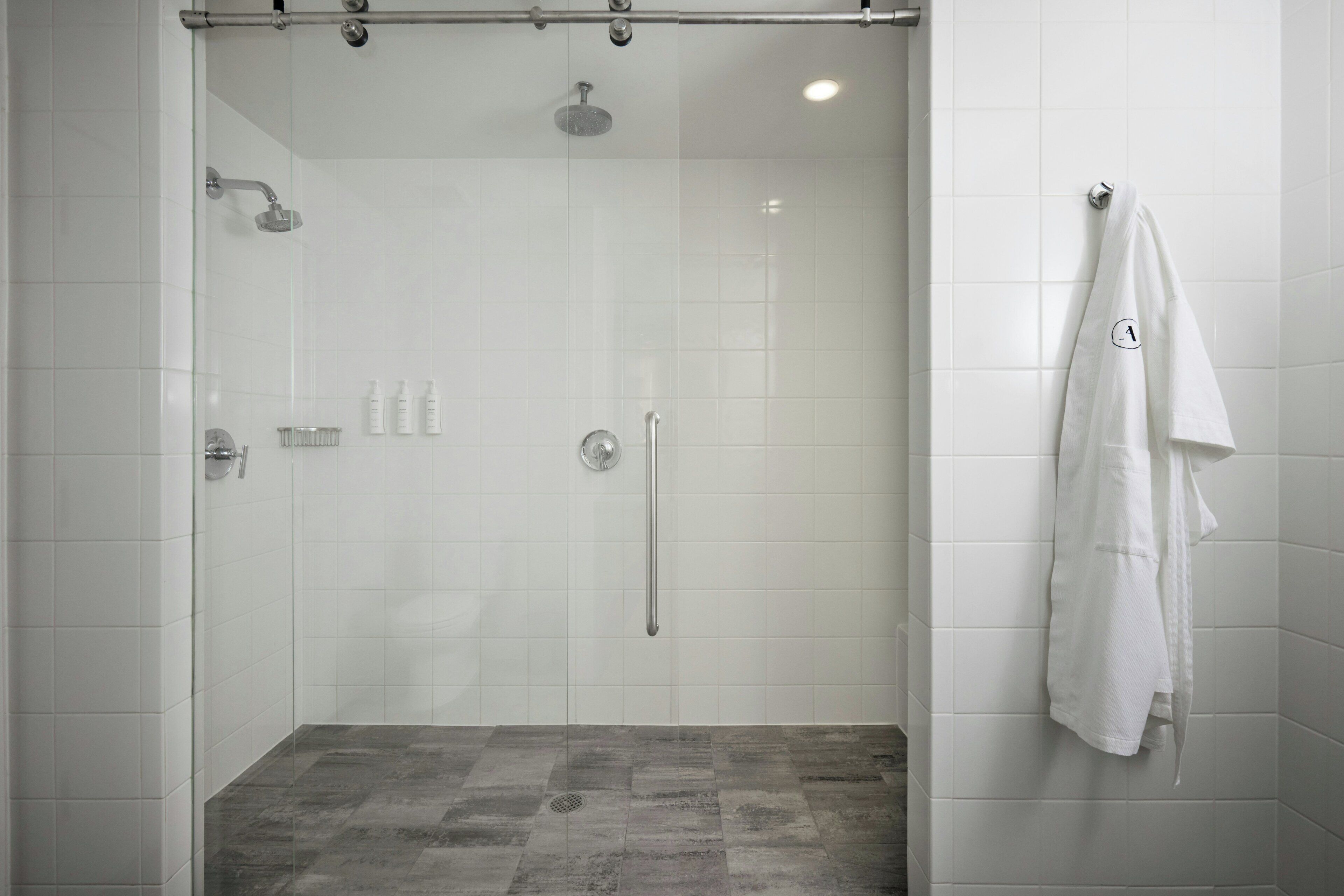 A glass-enclosed shower stall with a tiled floor, a towel hanging on the wall, and a showerhead.