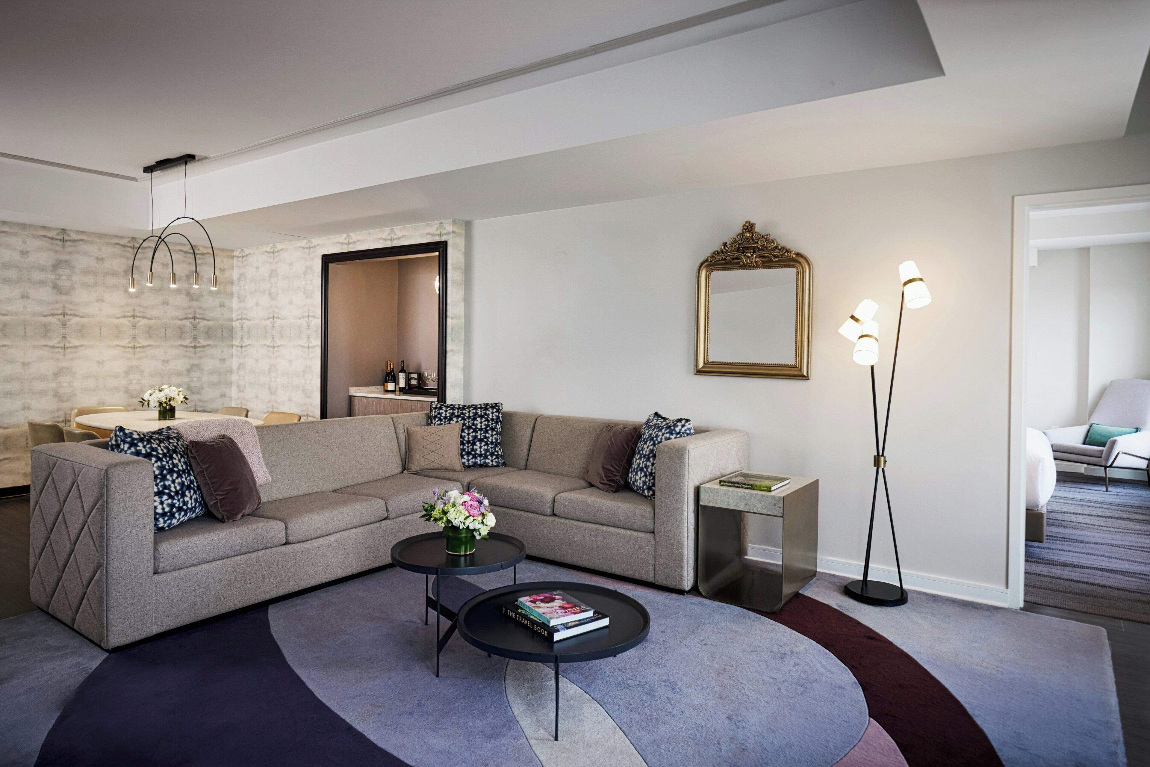 A modern living room with a sectional sofa, two coffee tables, a floor lamp, and a mirror.